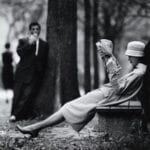 Woman-reclining-on-park-bench-reading-newspaper